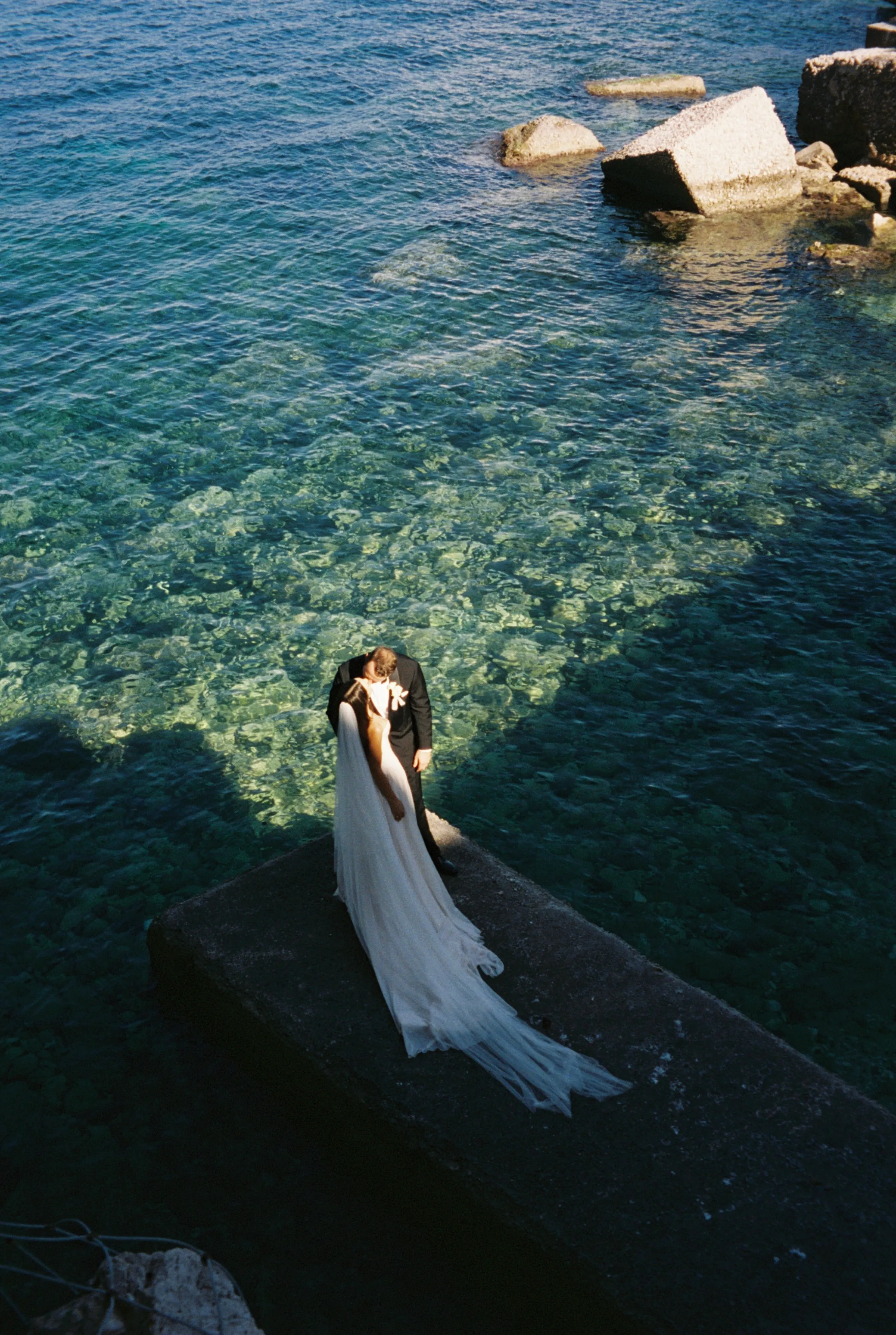 The couple kissing on a pier above turquoise water in Italy